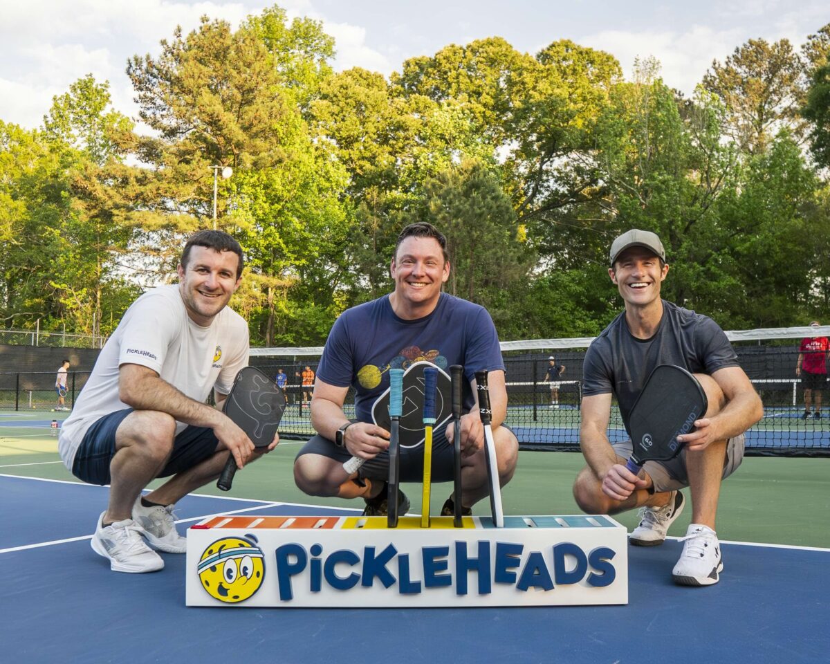 Group of three men on a pickleball court with a Pickleheads sign