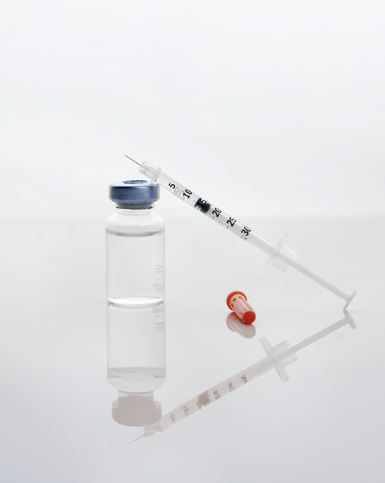 Syringe leaning on a clear glass container filled with medication