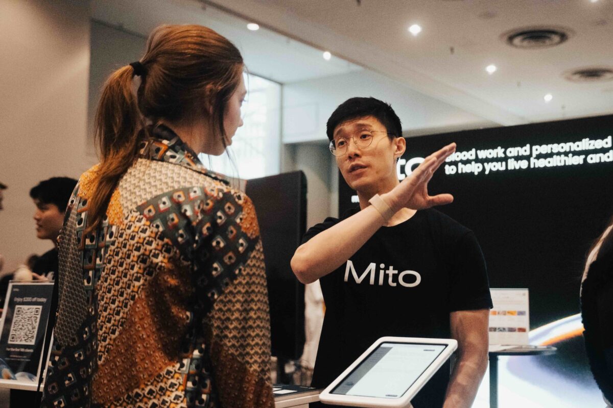 A man with a Mito shirt on is explaining something to a customer