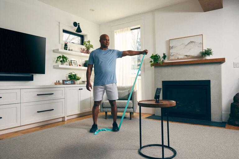 A man performing a single arm lateral raise with a resistance band in his living room
