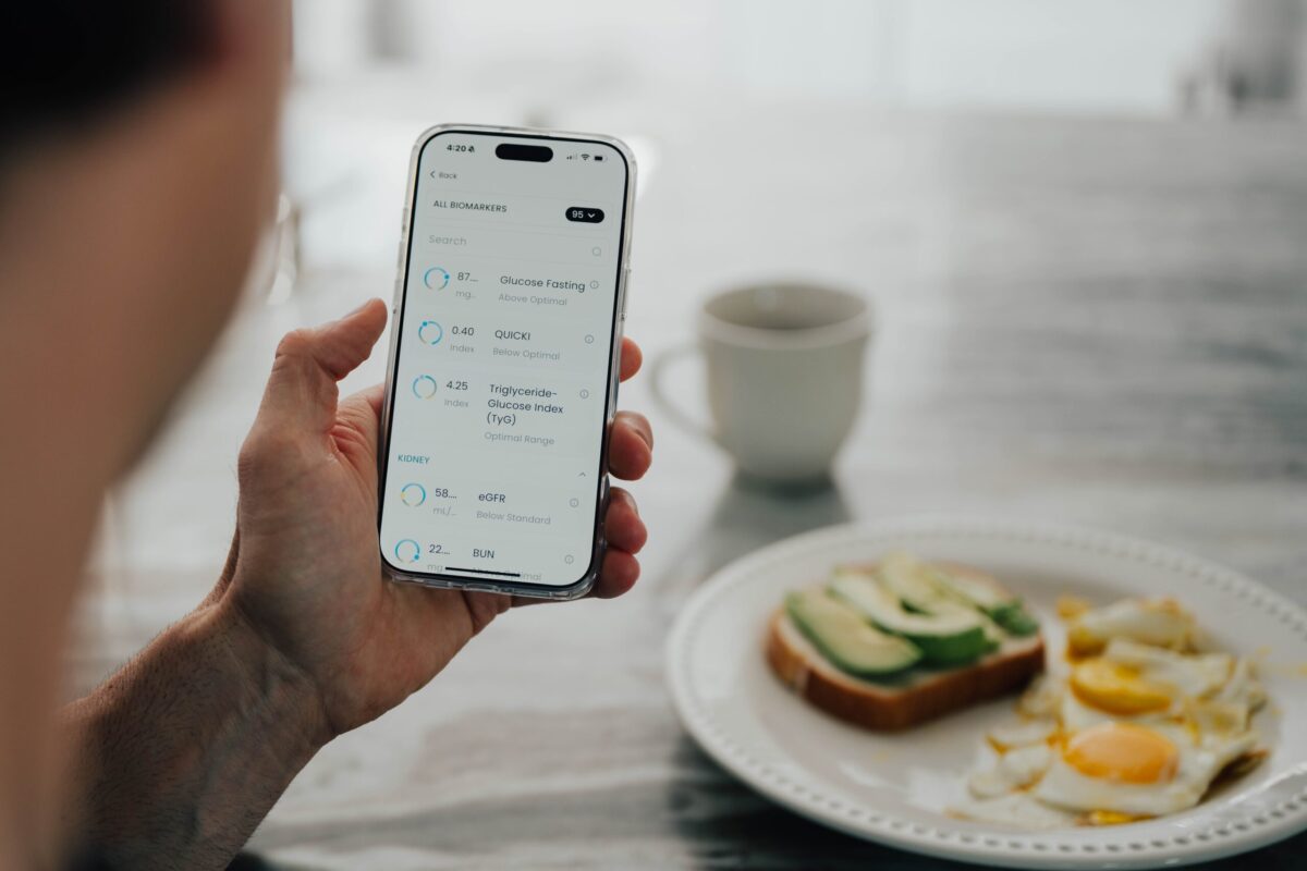 A person looking at biomarkers on their phone with breakfast and coffee plated on the table