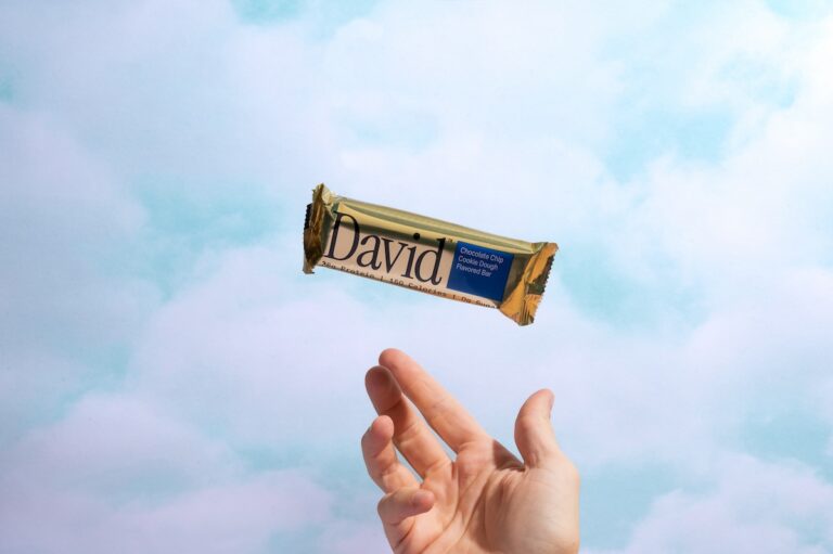 A hand tossing a David protein bar into the sky