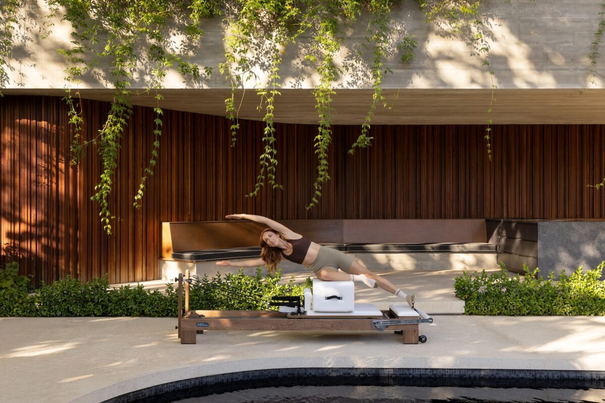 A woman performing a side bend on a Pilates reformer outdoors