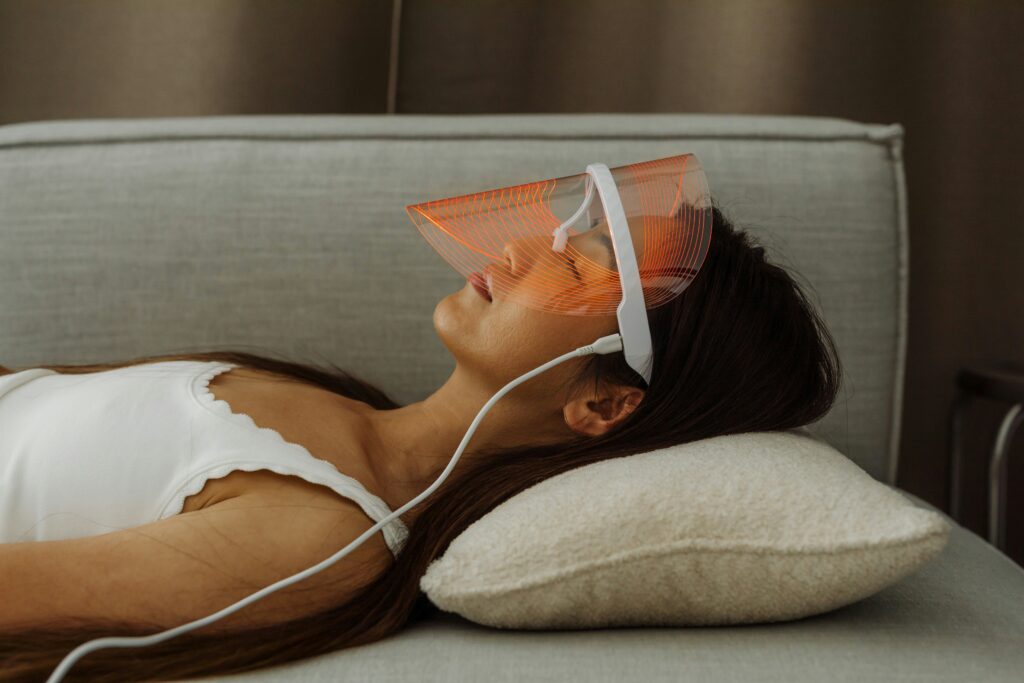 A woman laying on the couch with a red light mask on