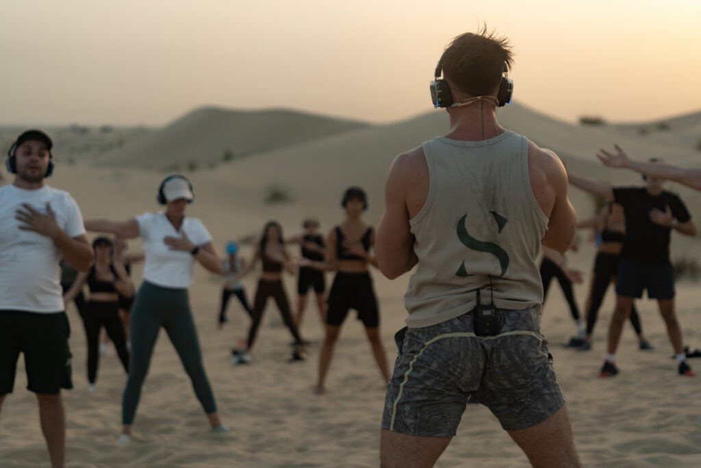 An instructor with headphones on leading a group experience in the desert