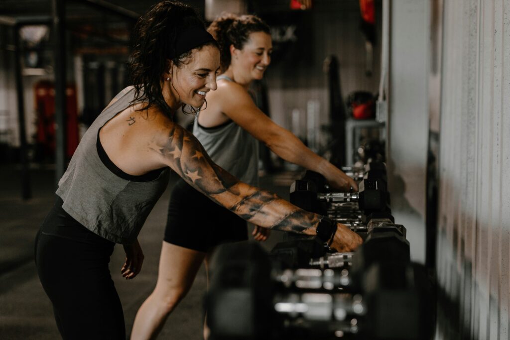 Two women reaching for dumbbells at the gym