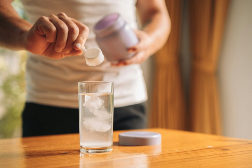 A person scooping a powdered supplement into a glass of water