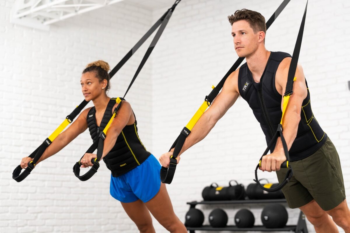A man and woman performing a TRX exercise with a weight vest