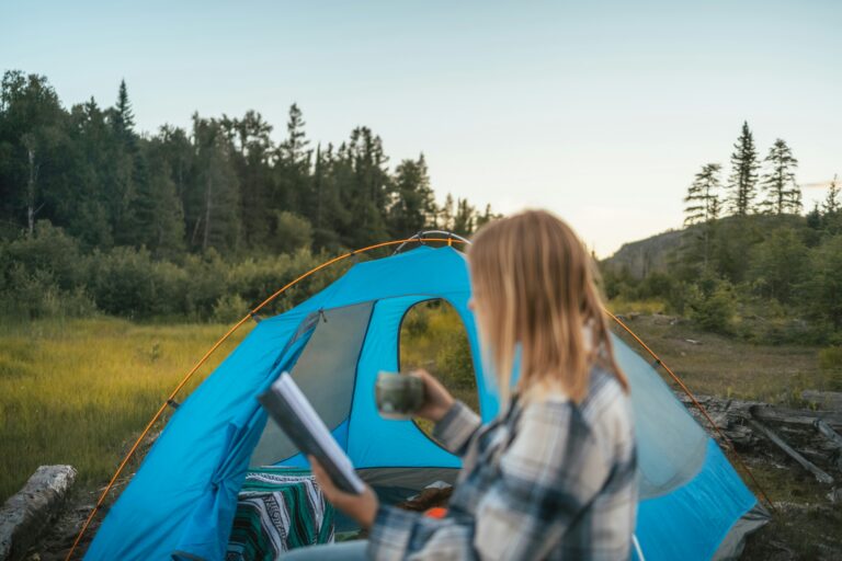Woman standing by a camping tent holding a mug and book