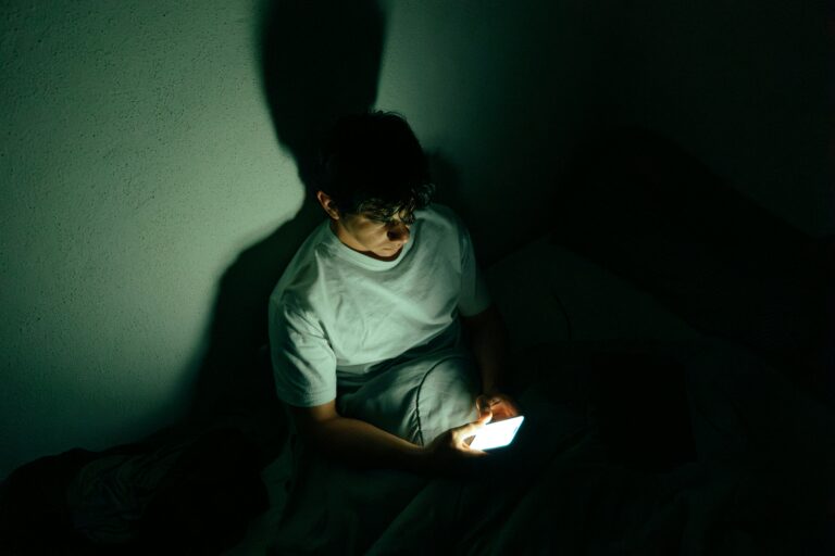 Man sitting in the dark alone looking down on a phone