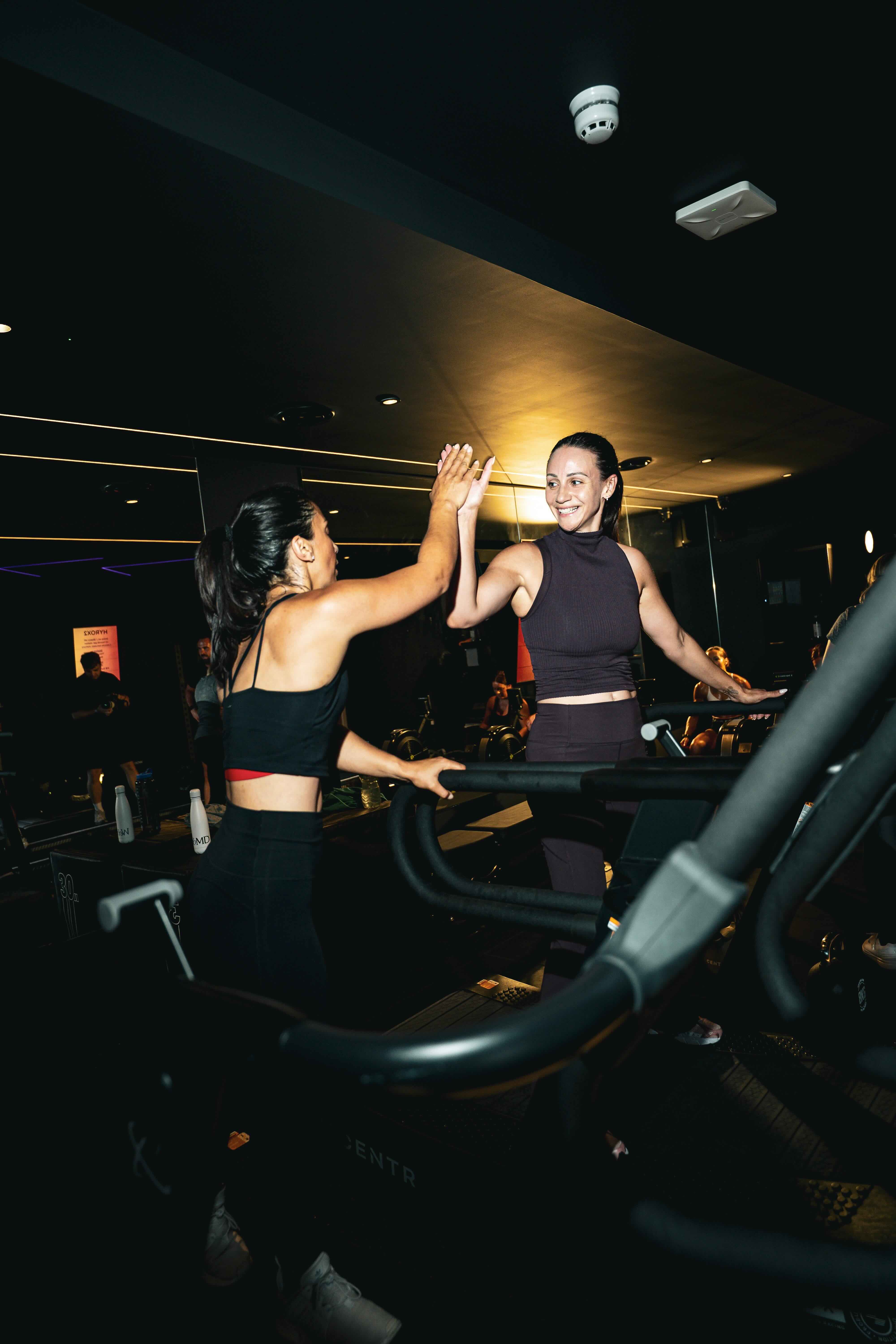 Two women on treadmills high-fiving each other