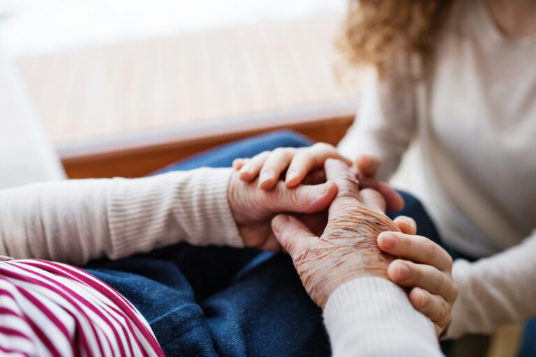 Unrecognizable girl with grandmother holding hands at home