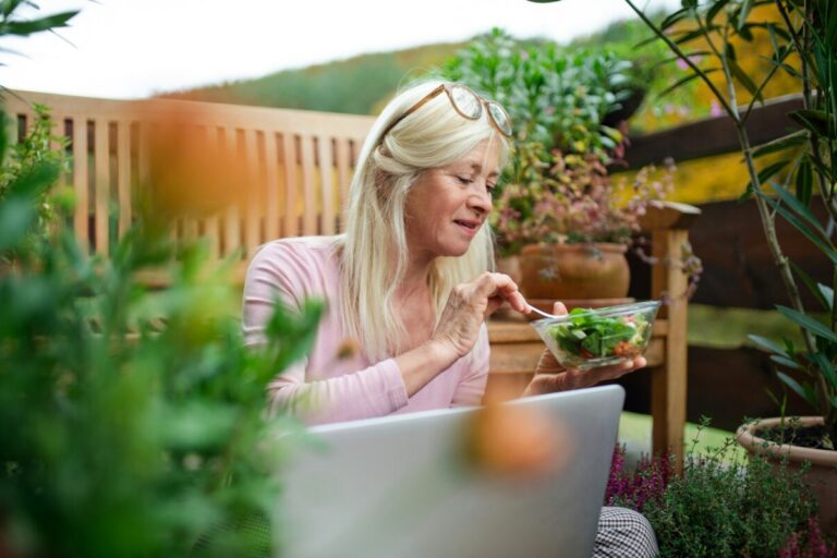 Midlife woman eating salad while on her computer